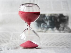 Close-up of a transparent hourglass with pink sand flowing, placed on a newspaper background.