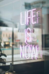 Urban scene with a glowing 'Life is Now' neon sign reflecting in a window, conveying a modern, motivational vibe.